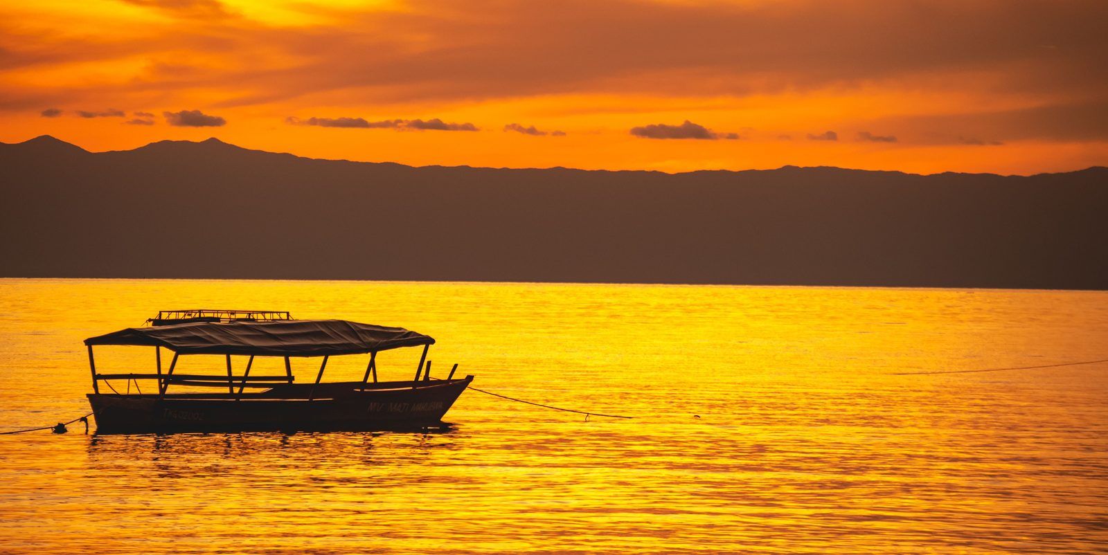Fishing boat silhouetted against an orange sunset over Lake Victoria at Ggaba