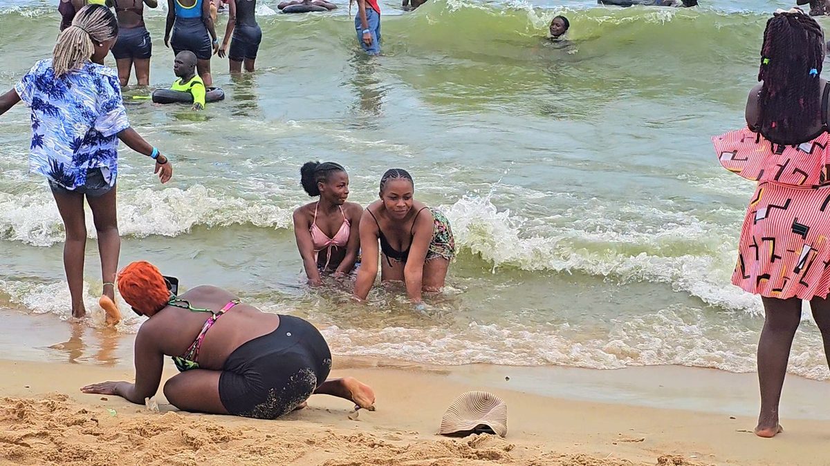 Crowd of people swimming and splashing in the waves at a sandy Ugandan lake beach